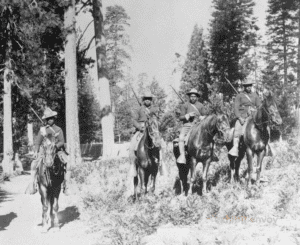 In a black-and-white photograph, four African American soldiers patrol Yosemite National Park while mounted on horseback.